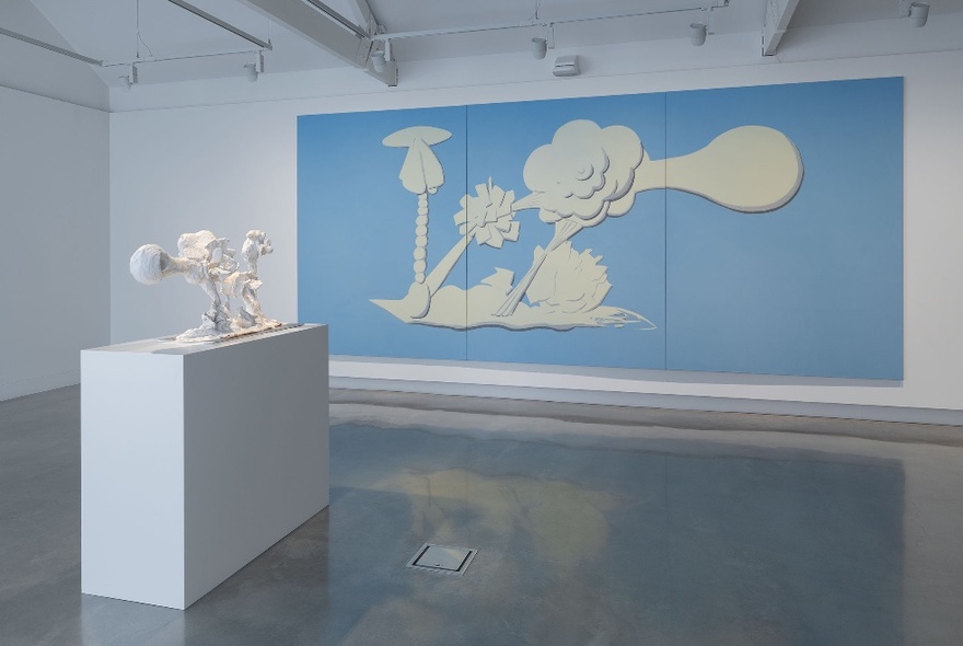 Large blue and white Wedgwood-inspired artwork panel on a white gallery wall, a white bench with white sculpture in the foreground.