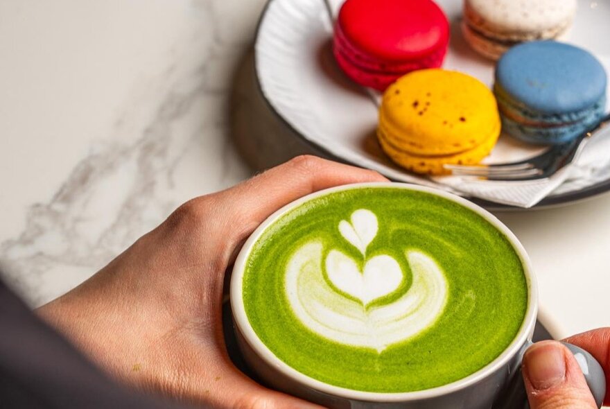 A green matcha latte and a plate of small coloured macrons.