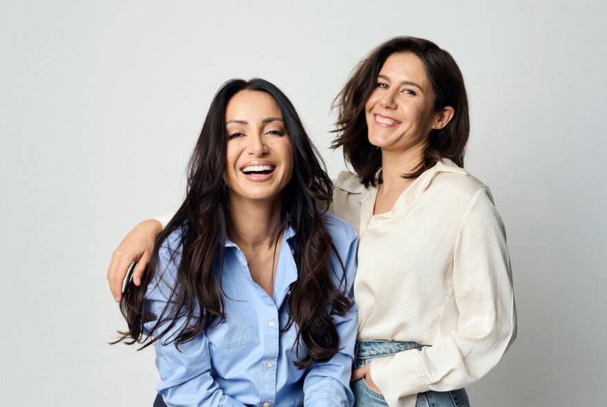 Jan Fran in a white shirt and Antoinette Lattouf wearing a pale blue shirt, smiling and casually posing in front of a white wall.