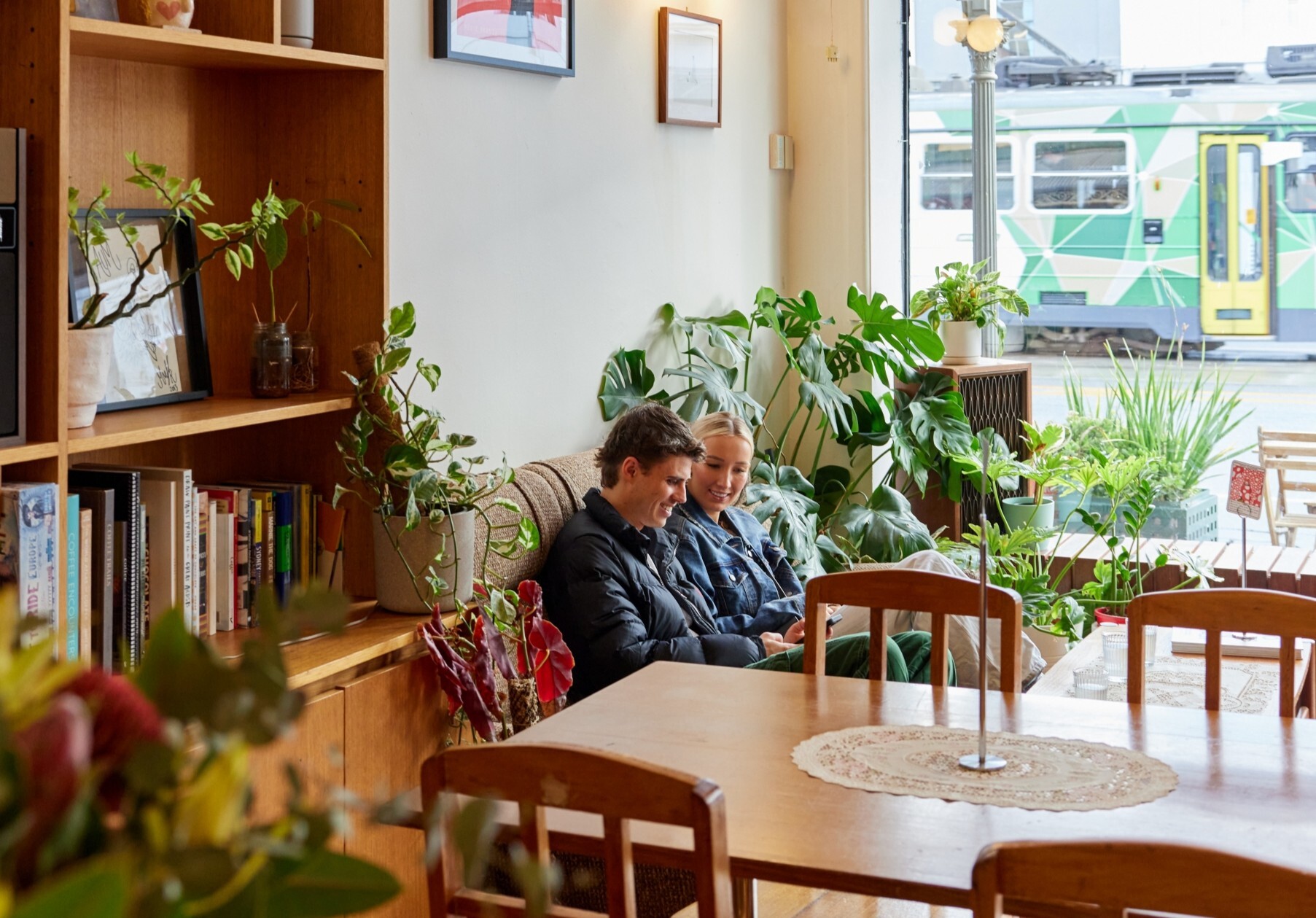 A couple sit in a leafy cafe chatting on a couch
