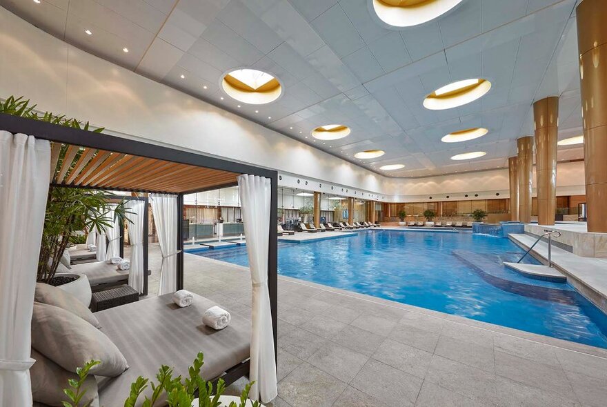 Indoor hotel pool with bathing cabanas with curtains and daybeds.