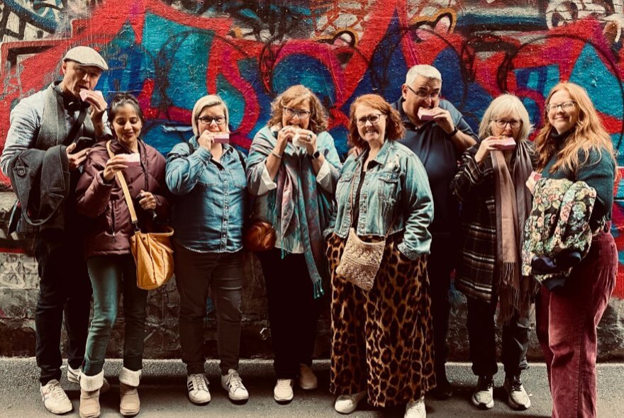 Walking group eating snacks next to a muralled wall.
