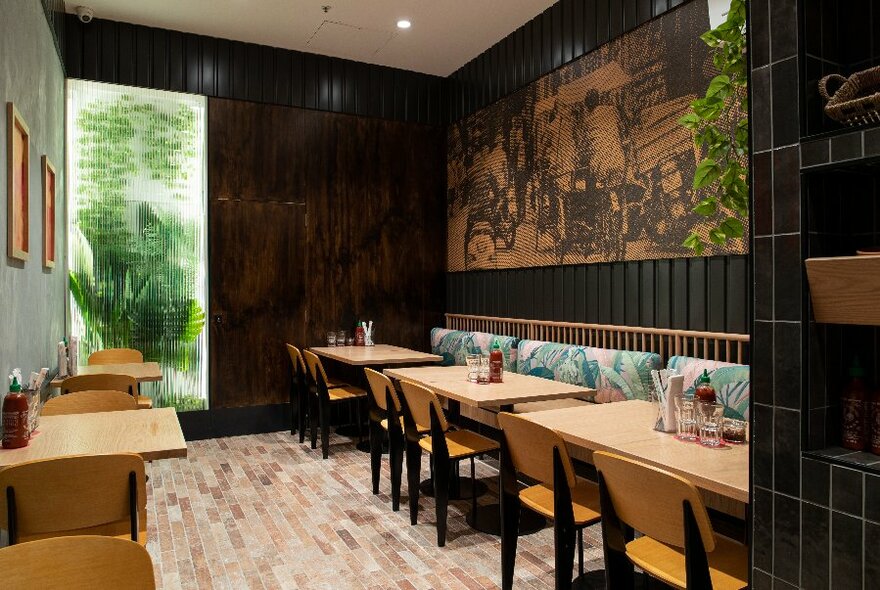 The interior of a neat restaurant with small wooden tables and green paintings on the walls. 