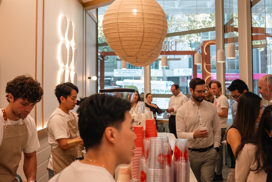 People queueing in a busy cafe with Japanese paper lantern andd barista staff.