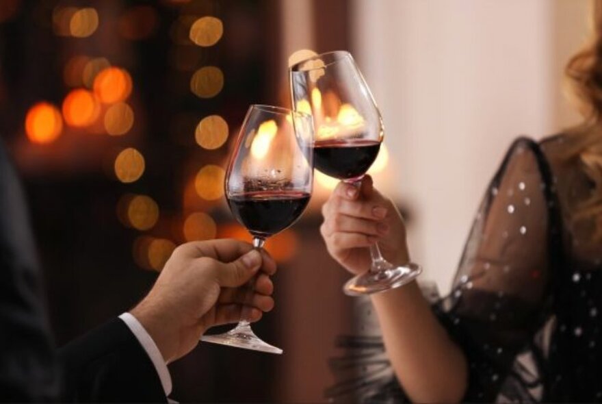 Two glasses of red wine raised in a toast together by two hands.