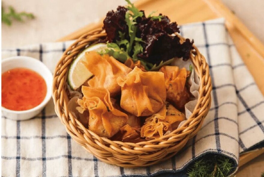 Dish of crispy fried dumplings in a basket with chilli sauce.