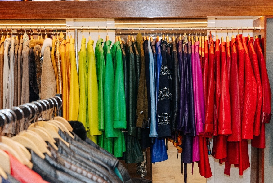 A colourful display of high end garments on a clothing rail, lined up according to their colour.