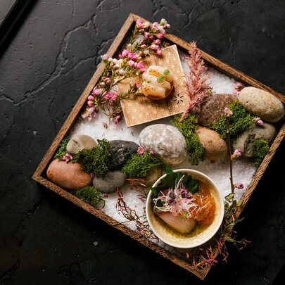 A Japanese dish presented on a tray with rocks and flowers.