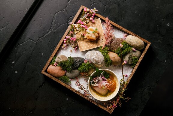 A Japanese dish presented on a tray with rocks and flowers.