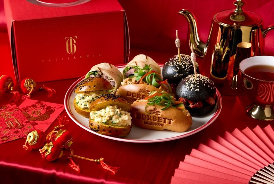 Afternoon tea selection on a plate against Chinese New Year red background with fan and ornaments.