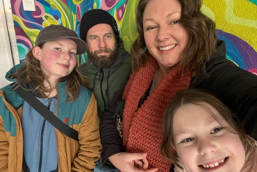 A family posing for a picture against a coloured wall, all looking happy. 