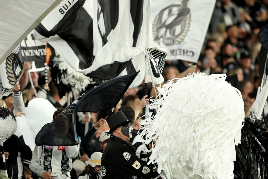 Collingwood AFL football fans in the stands with black and white flags and streamers. 