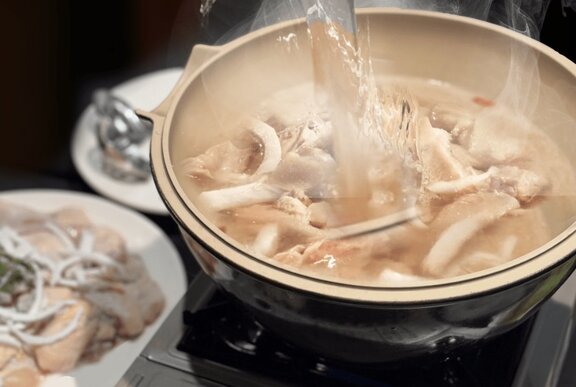 A chicken hot pot cooking on a small portable stove on a dining table in a restaurant.