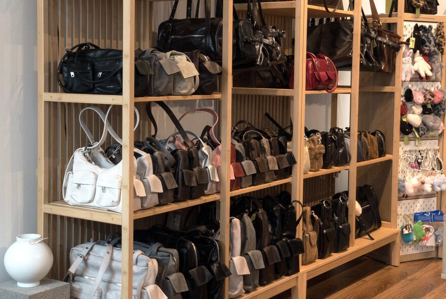 Rows of colour-coded leather handbags displayed on a wooden shelf in a shop.