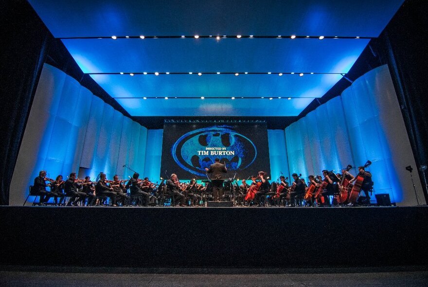 Huge screen showing Batman movie suspended over massed choir on stage.