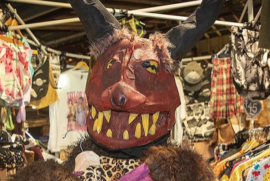 Large papier-mache model of a beast with bared teeth, standing in market stall with bags.