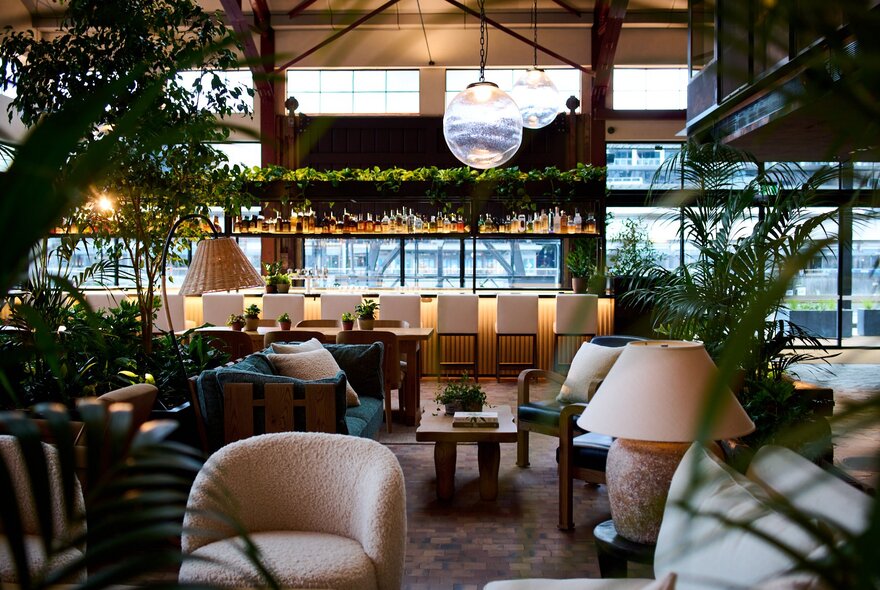 Crane Bar & Lounge on the ground floor of 1 Hotel Melbourne, with a bar at the back of the space, comfortable club chairs and low tables and lamps in the foreground.