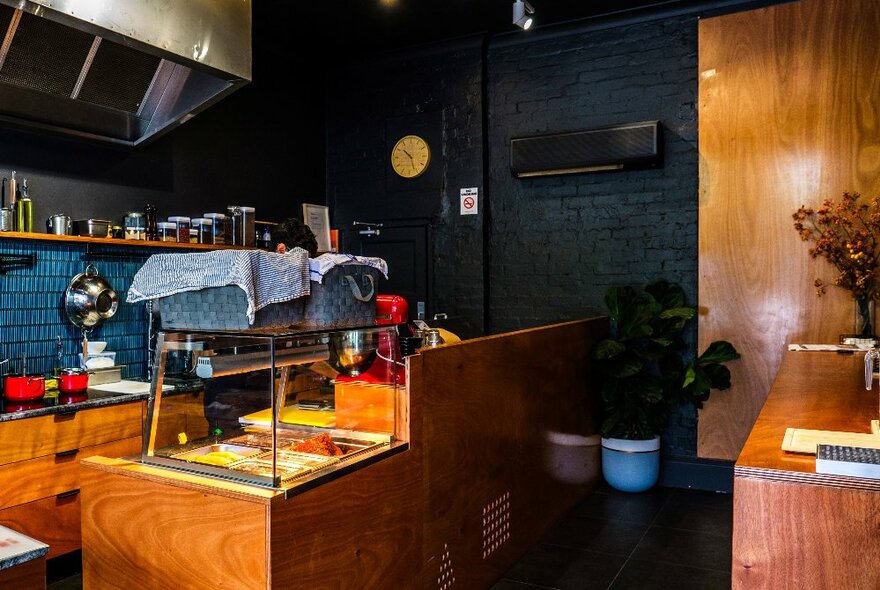 The interior of the small kitchen and service counter area at Rolld169 cafe in Kensington, with kitchen equipment on the walls and counter and food behind the glass display.