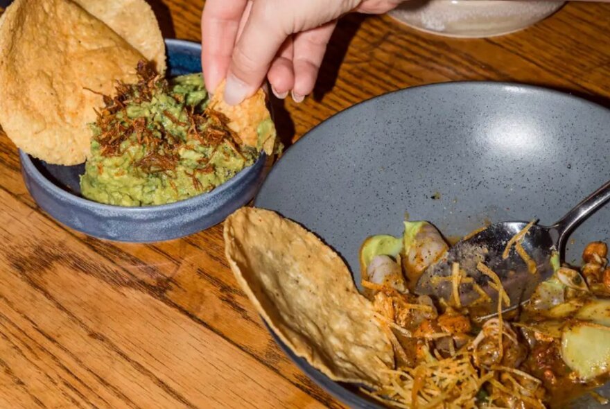 Hands dipping chips into guacamole.