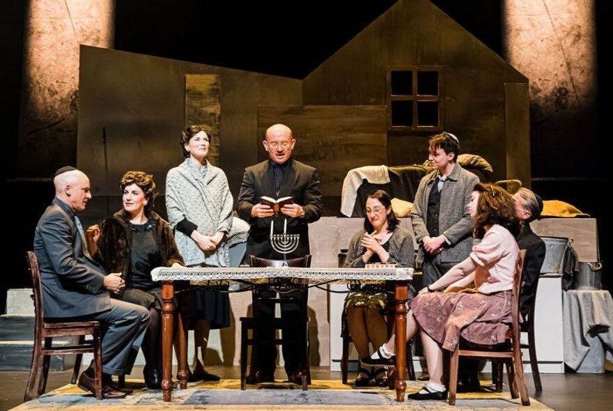 Cast on stage seated around a table with menorah.