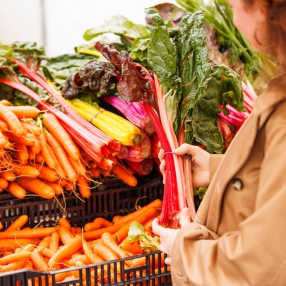 Person holding a large bunch of fresh rhubarb with carrots at an outdoor market stall.