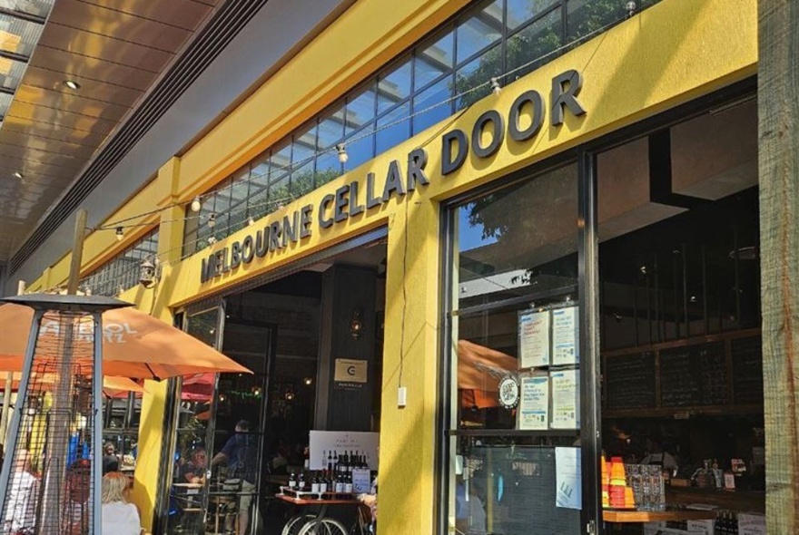 The yellow-painted entrance to Melbourne Cellar Door, with orange umbrellas and patio heaters out the front.