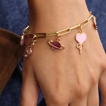 A hand wearing a goldcharm bracelet with a planet, and heart. 