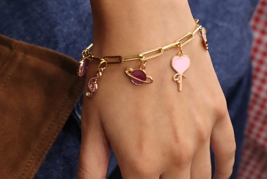 A hand wearing a goldcharm bracelet with a planet, and heart. 