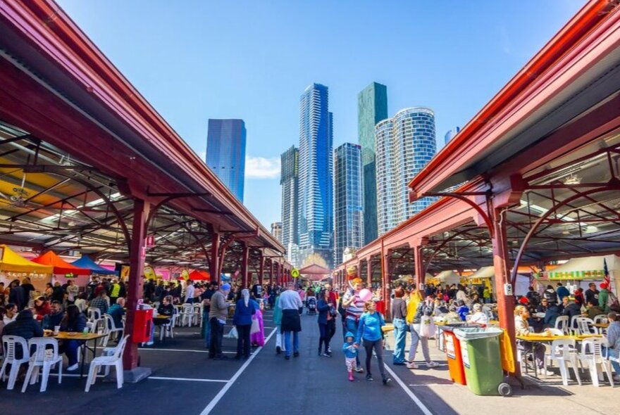 People walking around colourful market stalls on a sunny day in the city.
