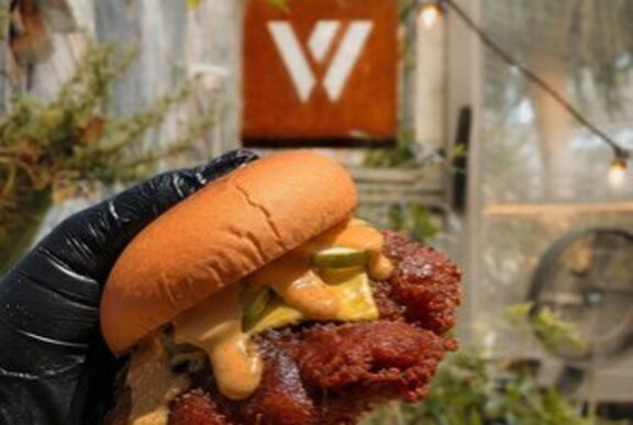 A gloved hand holding up a cheeseburger in front the of white W sign indicating Whitehart Bar.