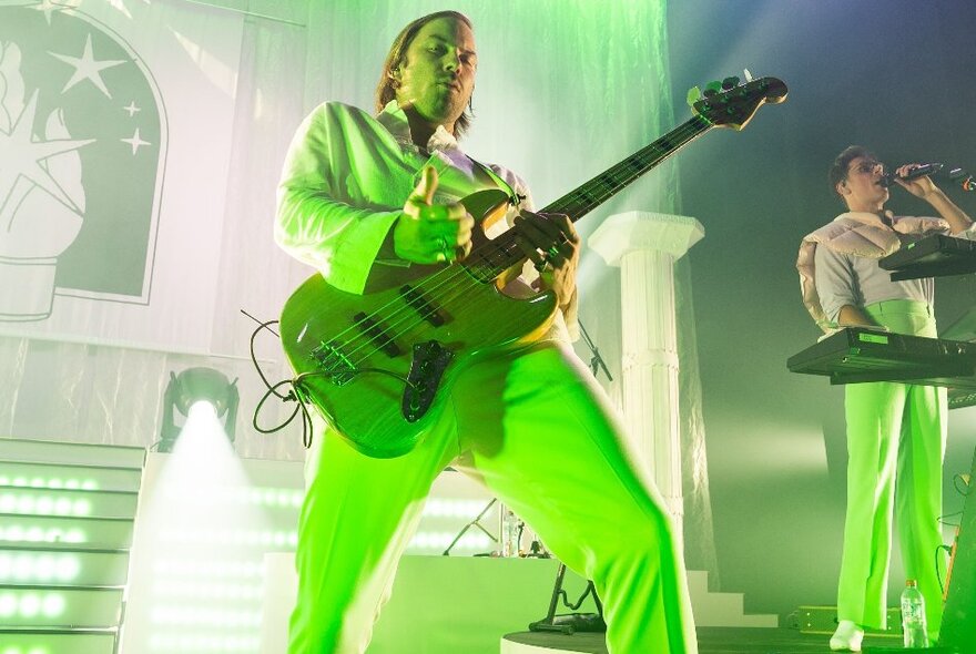 A lead guitarist dressed in lime green rocking out on stage. 