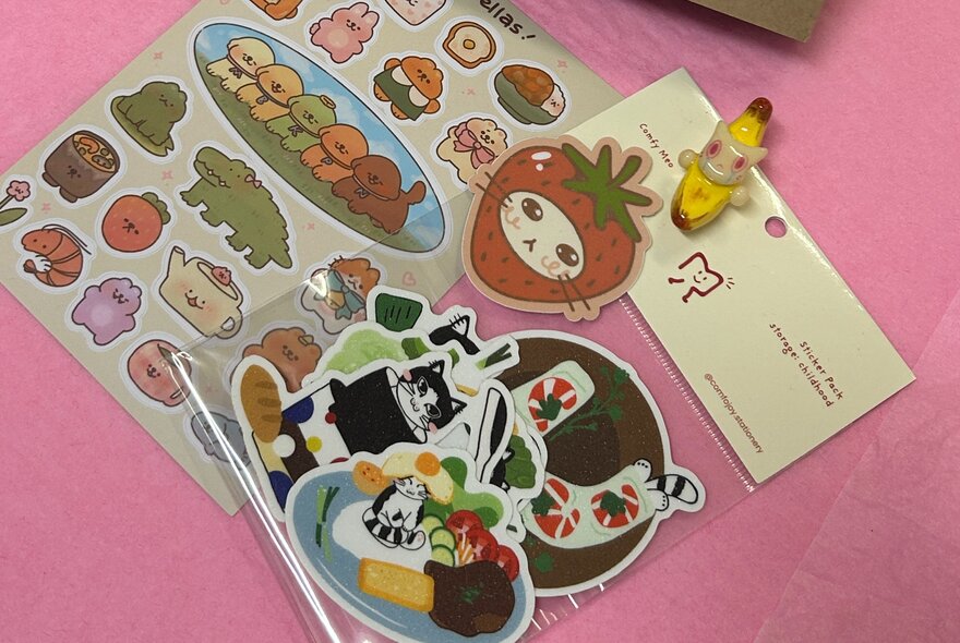 Looking on casually arranged sheets of cat stickers on a pink surface. 