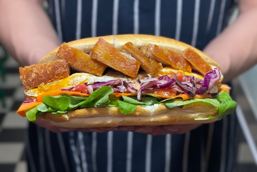 Overflowing baguette held up against blue and white striped apron.