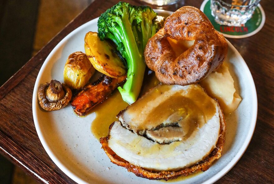 A roast pork dinner with broccoli, potato, carrot, gravy and a Yorkshire pudding.