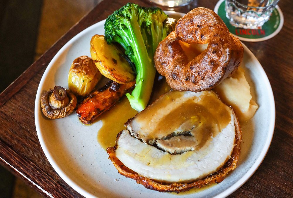 A roast pork dinner with broccoli, potato, carrot, gravy and a Yorkshire pudding.