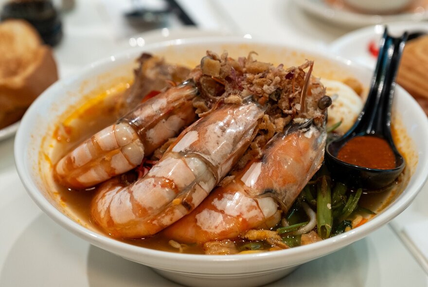 A bowl of laksa with giant prawns in it.
