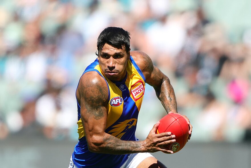 A West Coast Eagles AFL football player running with the ball in a stadium during a footy match.