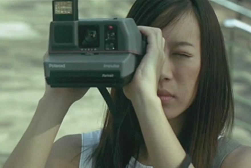 A still image from the movie Shutter showing a woman taking a photo with an Instamatic camera.