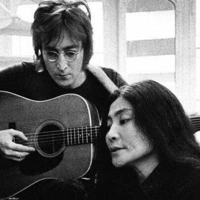 A black and white image of John Lennon playing guitar behind Yoko Ono
