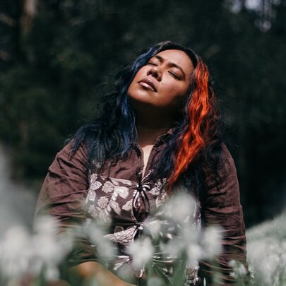 Singer Fatai standing outdoors, her face looking towards the sky with her eyes closed, she wears a jackets and has long dark hair.