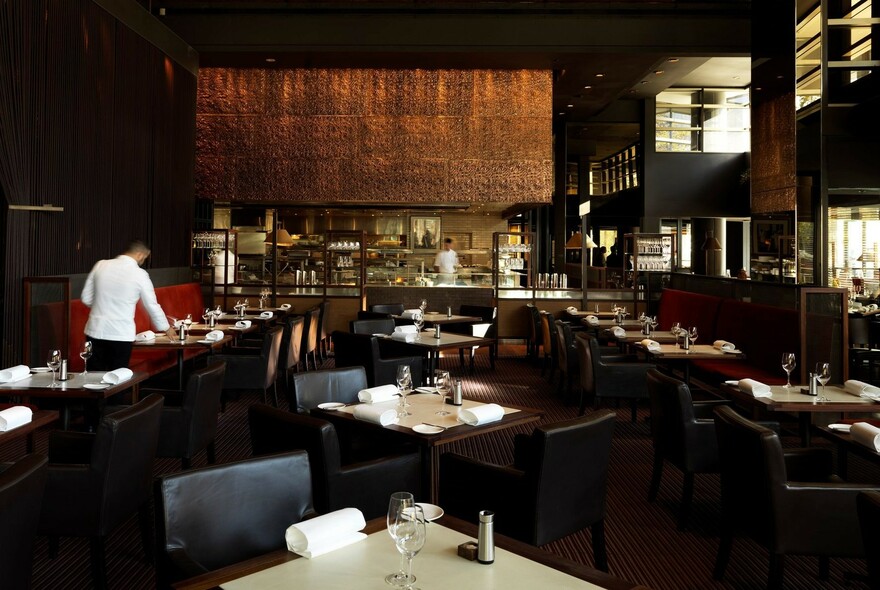 Dramatically lit dark restaurant with tables chairs, and a waiter setting a table.