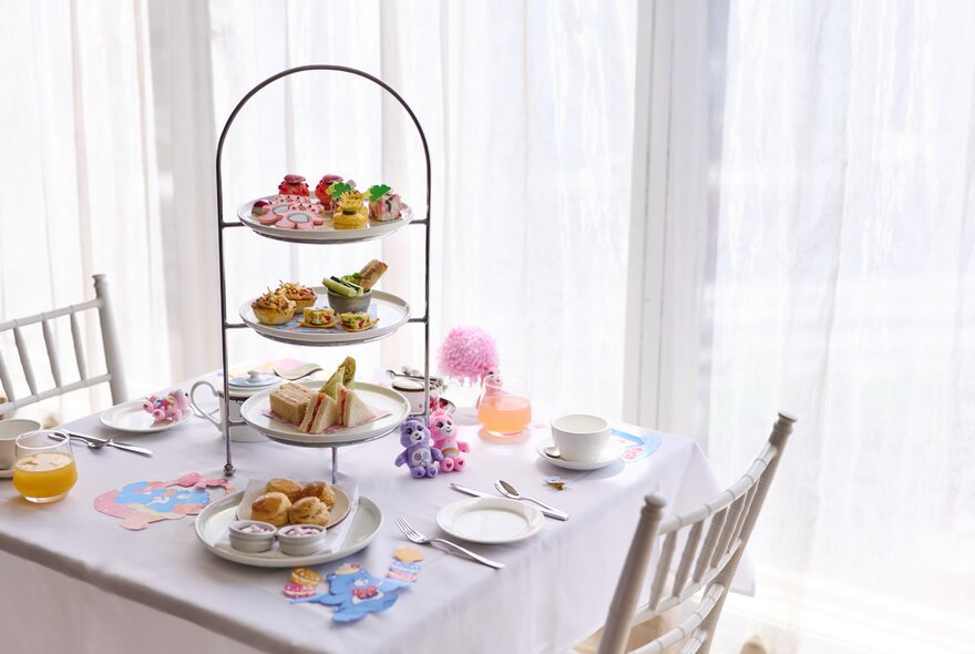 A table set for two with a tiered serving platter filled with Care Bears themed high tea treats.
