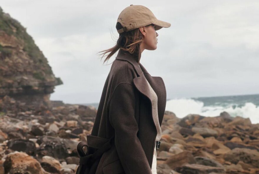 A model wearing a chocolate brown wool coat at the beach.