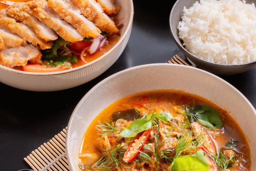 Several bowls of food including an Asian style soup, sliced katsu chicken and plain rice. 