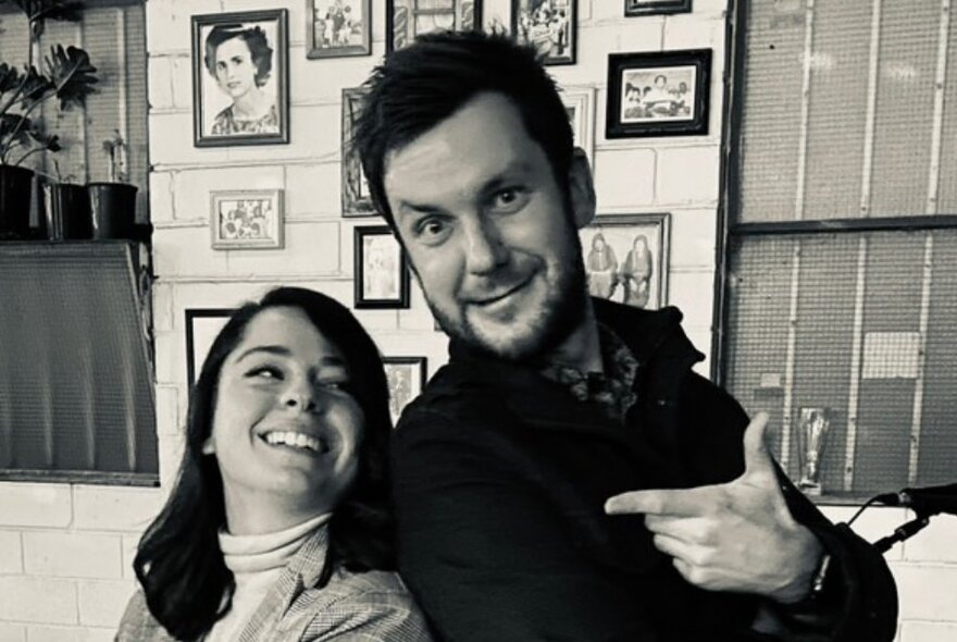 A black and white image of a man and woman posing back-to-back, the man pointing at the woman and joking around. 