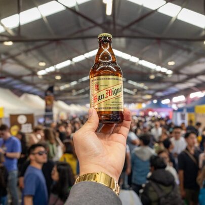A bottle of San Miguel beer raised at market event Pinoy Octoberfest, held at the Queen Victoria Market, with a blurred crowd in the background.