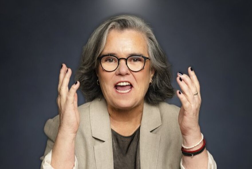 Portrait of American comedian, Rosie O'Donnell, with her hands up mid-gesture and mouth open, talking.