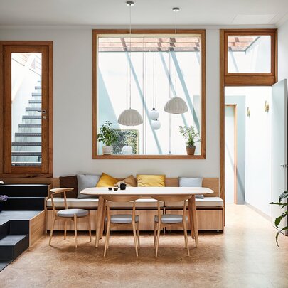 A modern room space with three windows of different shapes, a dining area and a plant. 