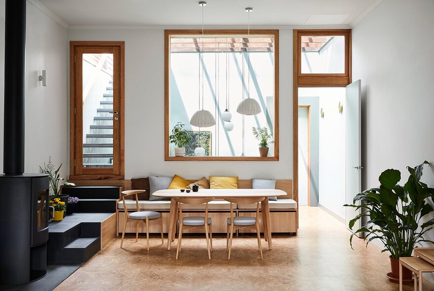 A modern room space with three windows of different shapes, a dining area and a plant. 