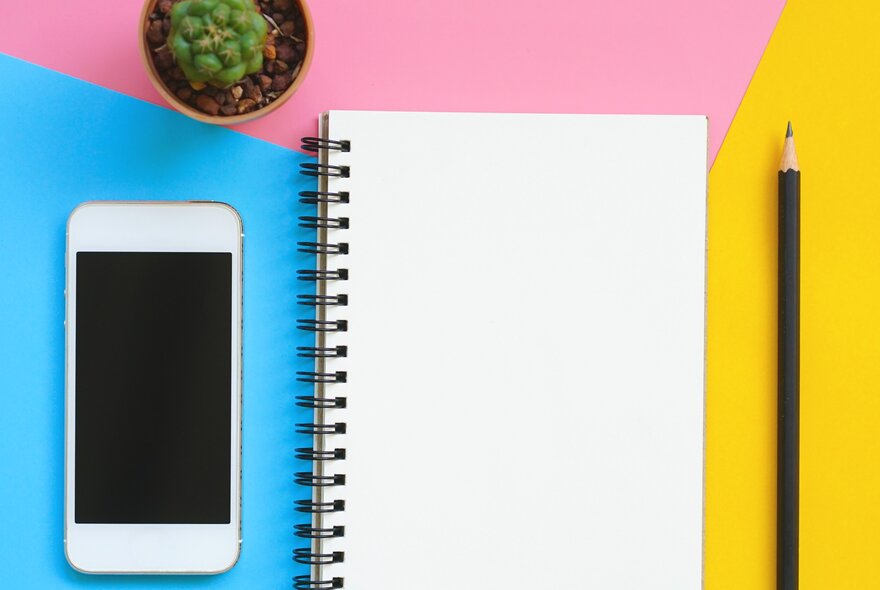 A spiral-bound blank workbook next to a closed mobile phone and pencil.